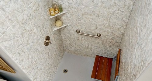 The interior of a no-threshold shower with a wooden bench seat, grab bar, and corner caddy.