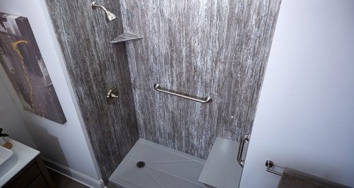 A walk-in shower with gray acrylic wall surrounds, grab bars, and a bench seat. 